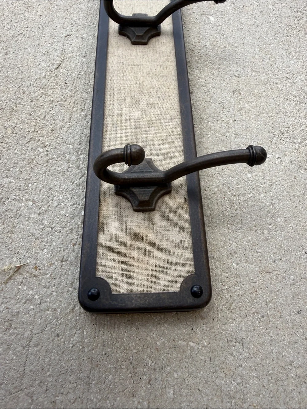 Hook rack features a dark bronze frame with a light-colored linen backing